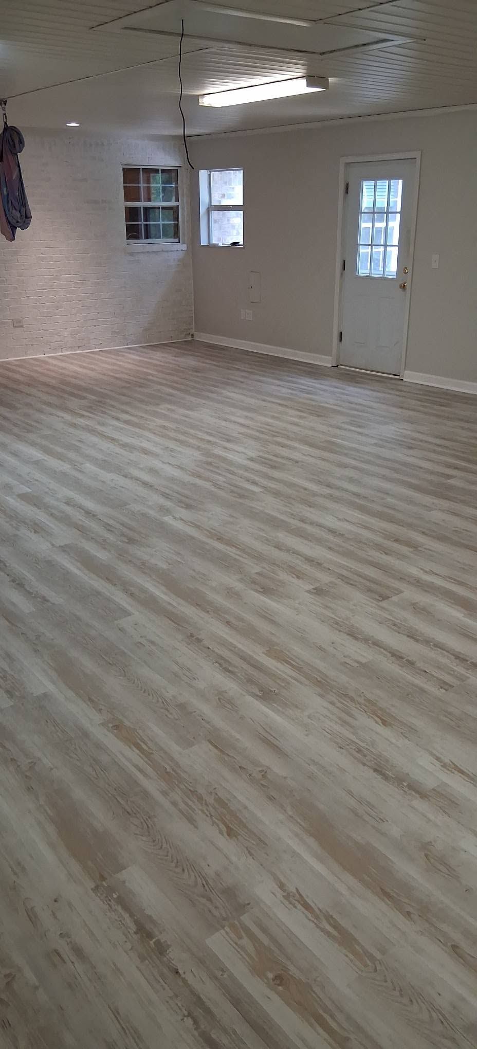 Empty room with light wood flooring, white walls, ceiling lights, and windows and a door on the far wall
