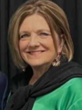Woman smiling in a green top with a black sweater draped over her shoulders against a dark background