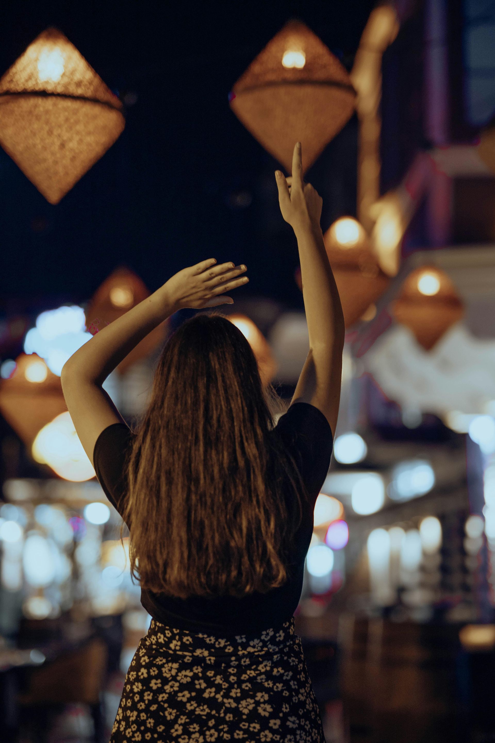 Person with raised arms in a lantern-lit street at night