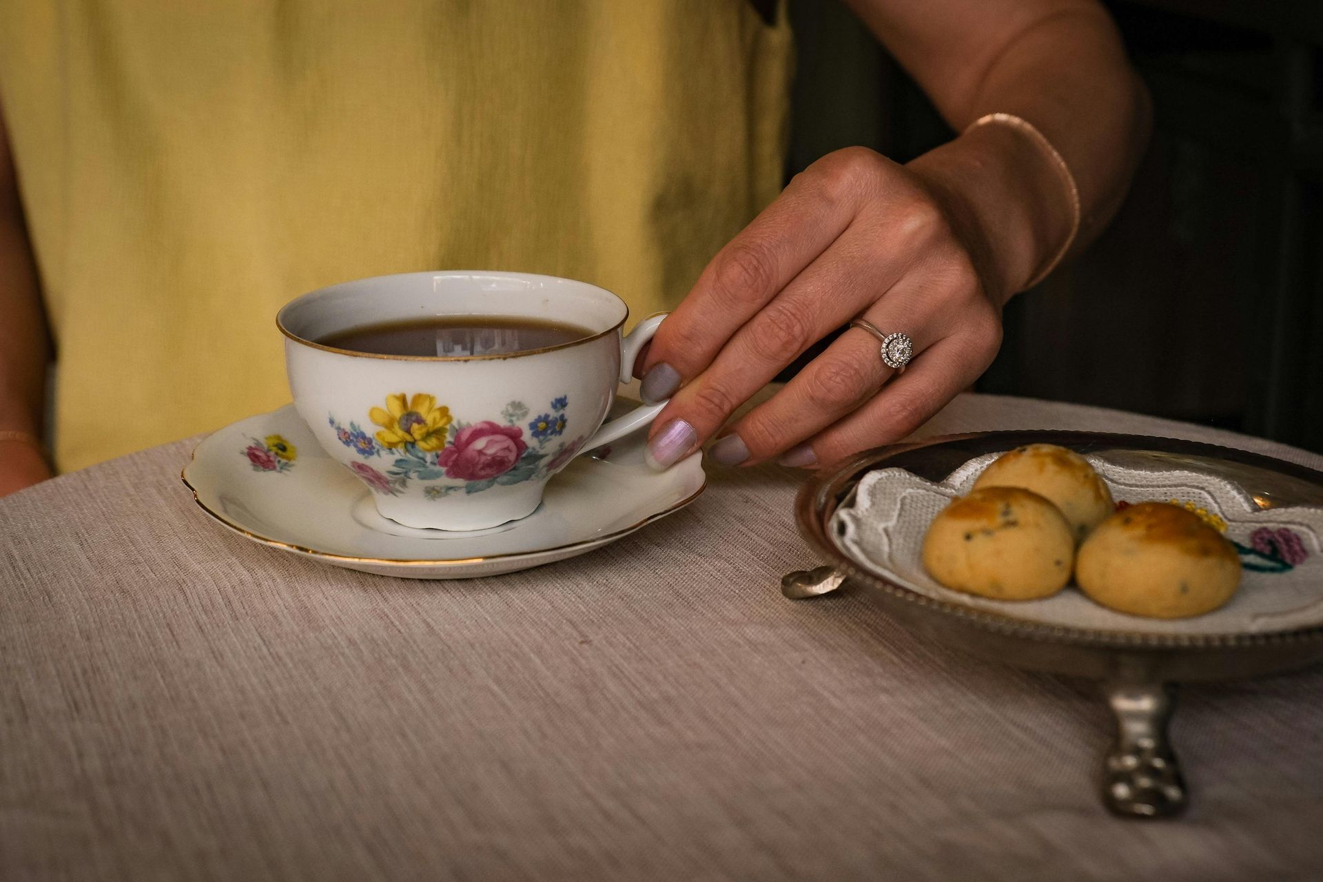 Hand placing a teacup on a saucer beside a plate of cookies on a table