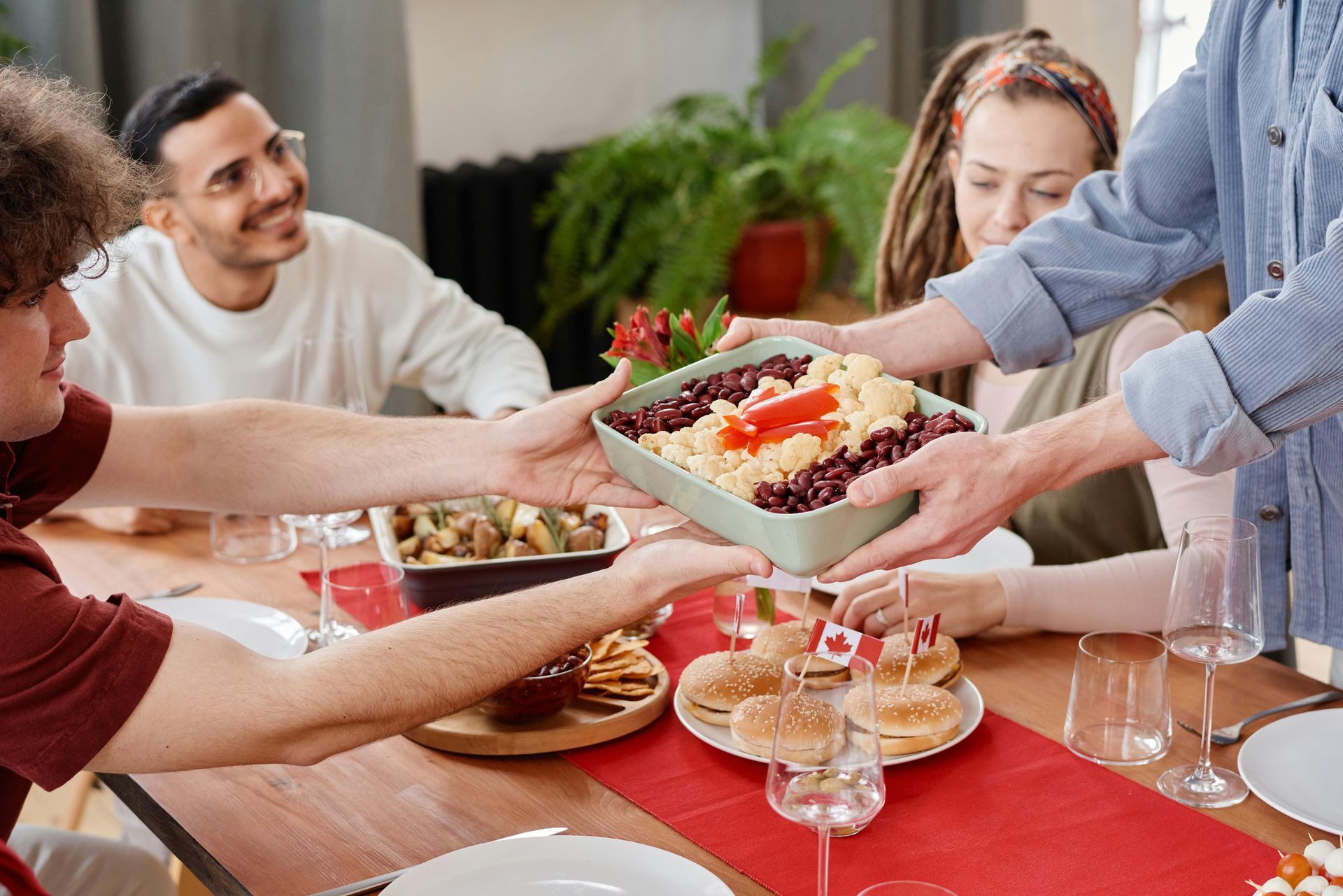 Friends serving food at a table with a red runner during a shared meal