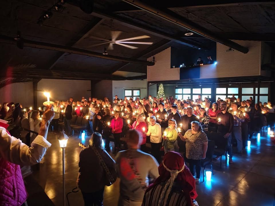 Crowd gathered indoors holding lit candles during a vigil or memorial event