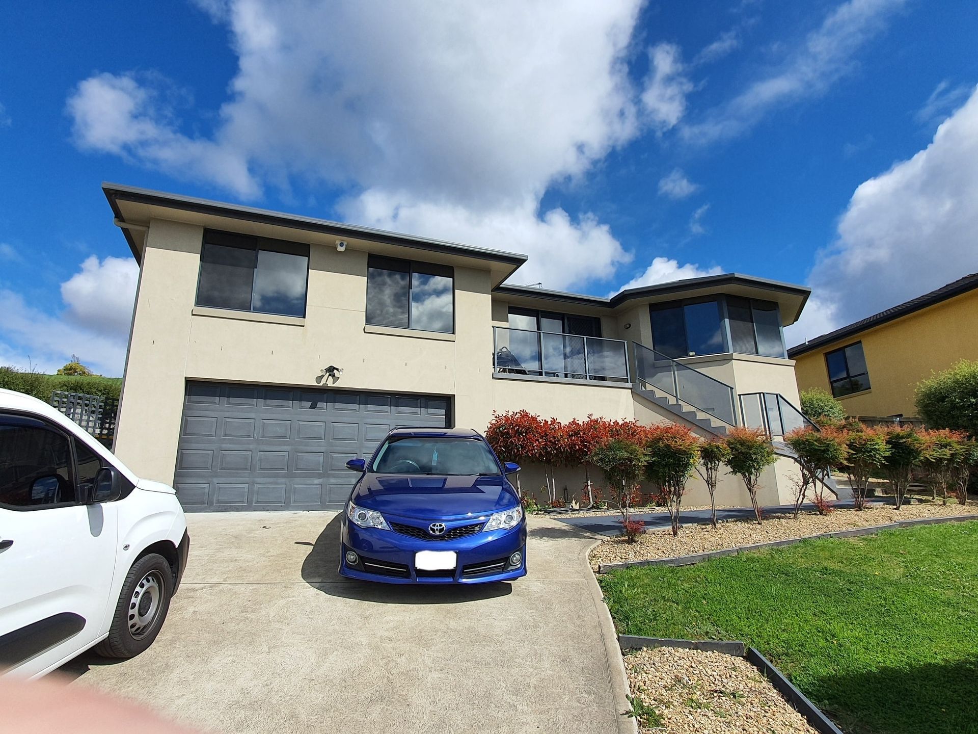 A Two-story Tan House With a Gray Garage Door and a Blue Car Parked — Shmick Tinting & Vinyl in North Hobart, TAS