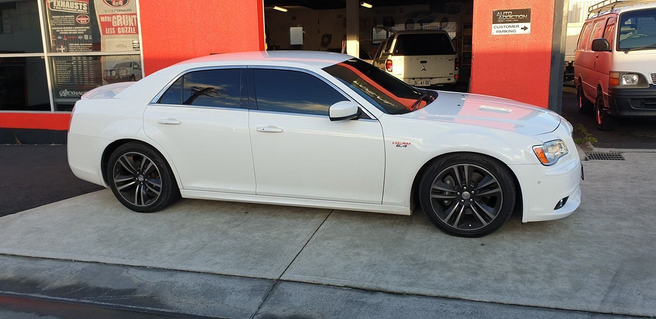 White sports sedan parked outside a red storefront, side view on a sidewalk.