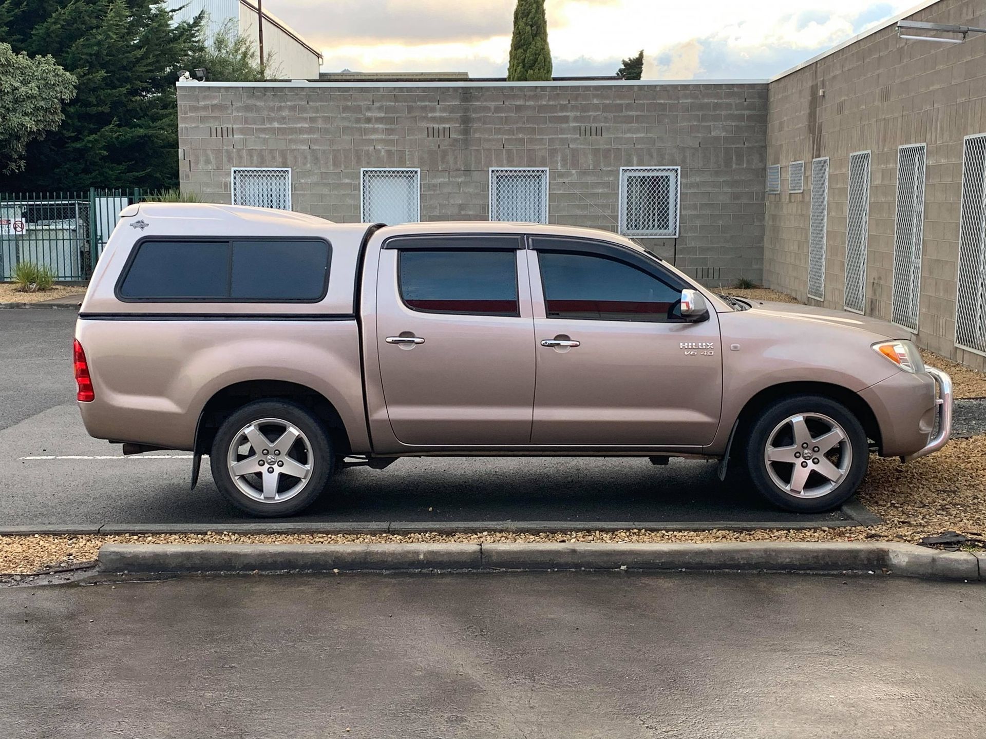 Tan SUV parked beside a brick building on a wet street, with a canopy over the bed.
