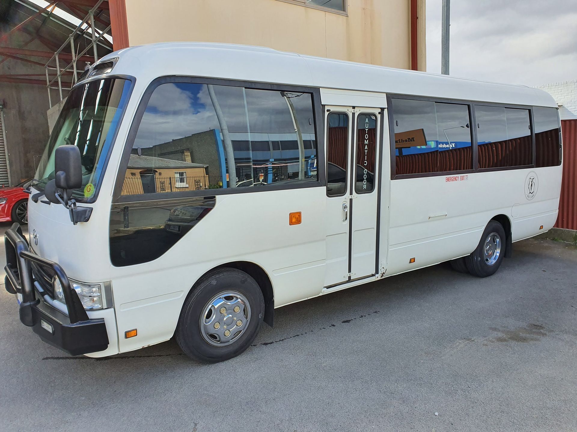 White passenger minibus parked on a street beside a building.