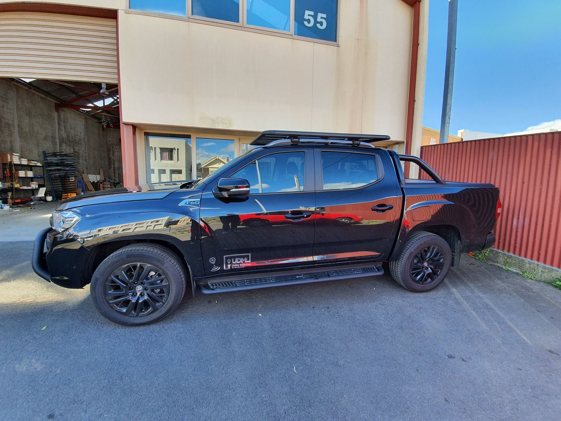 Black SUV parked beside a building with an open garage door and red fence