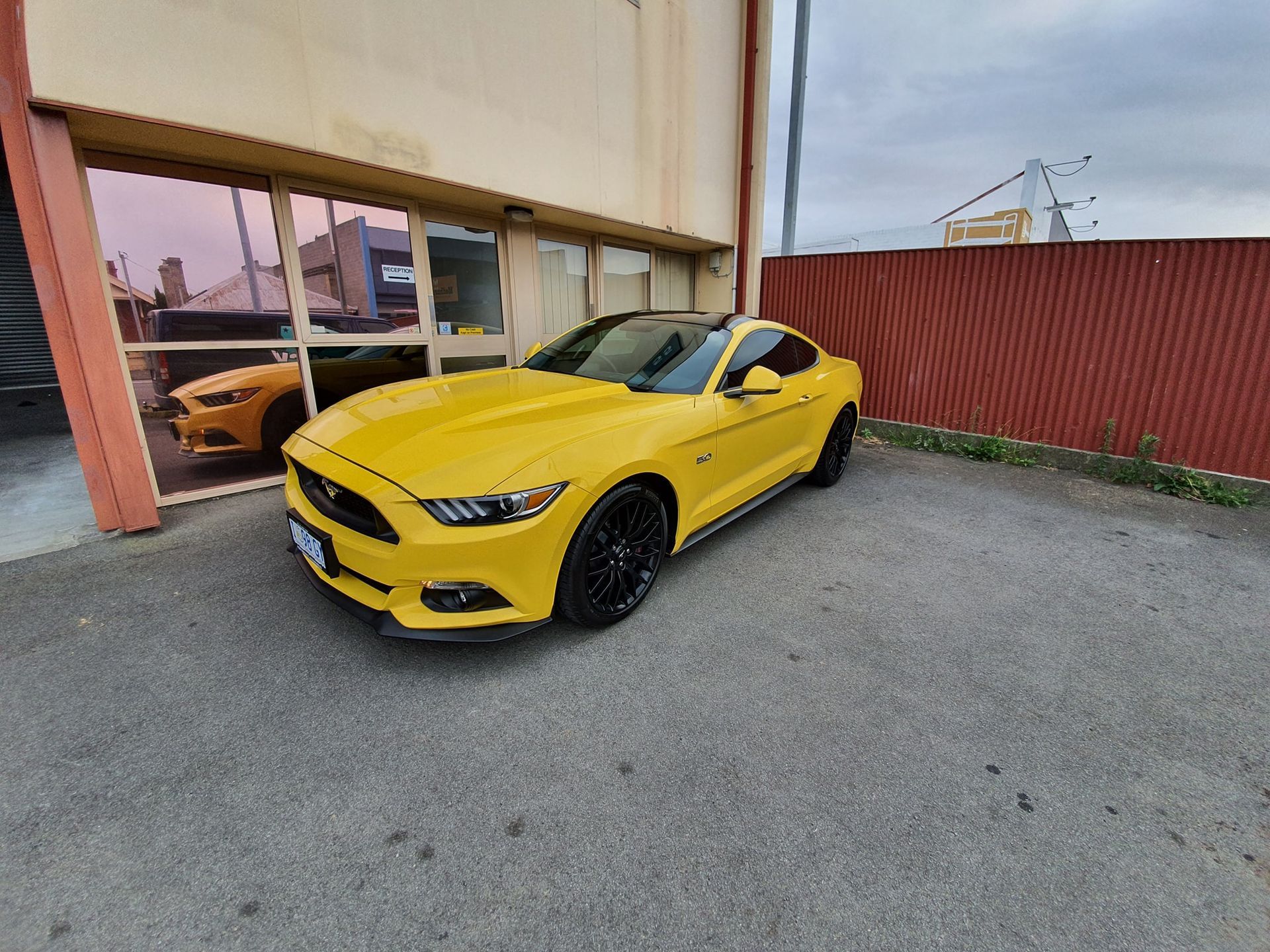 A Bright Yellow Ford Mustang Coupe Parked on Asphalt in Front of a Building — Shmick Tinting & Vinyl in North Hobart, TAS