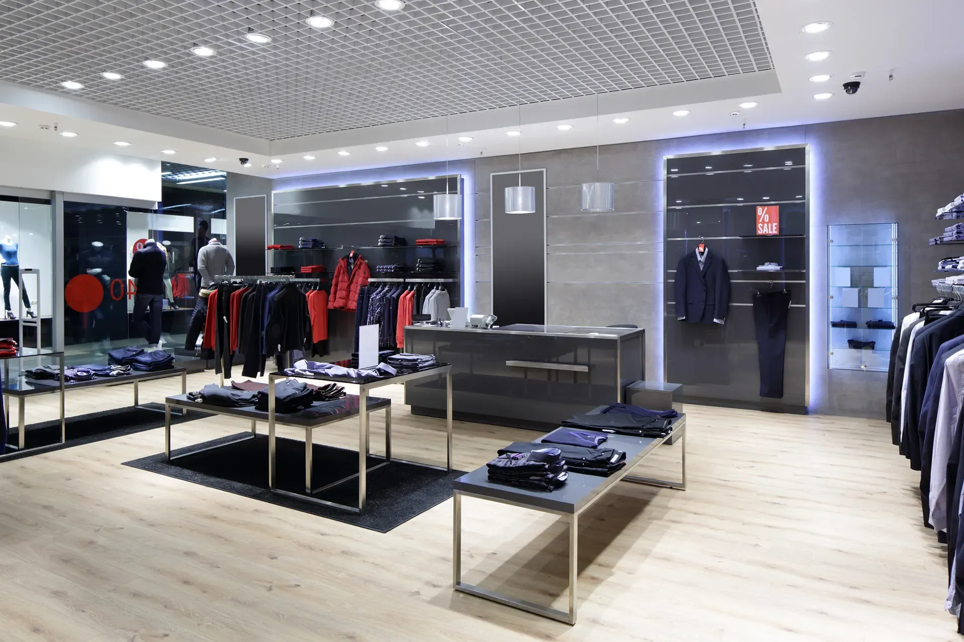 Clothing store interior with clothing displays, overhead lighting, and gray and black accents.