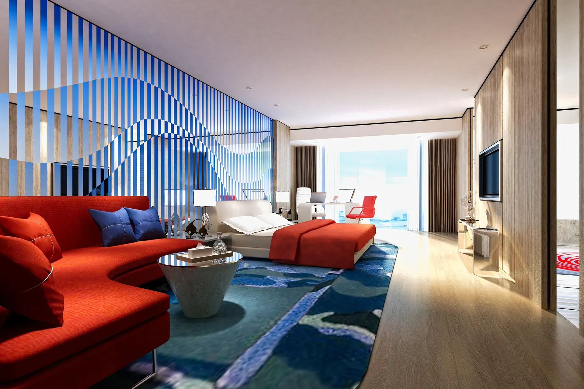 A vibrant hotel suite features a red sofa, blue patterned rug, and white bed with a view of the sea.