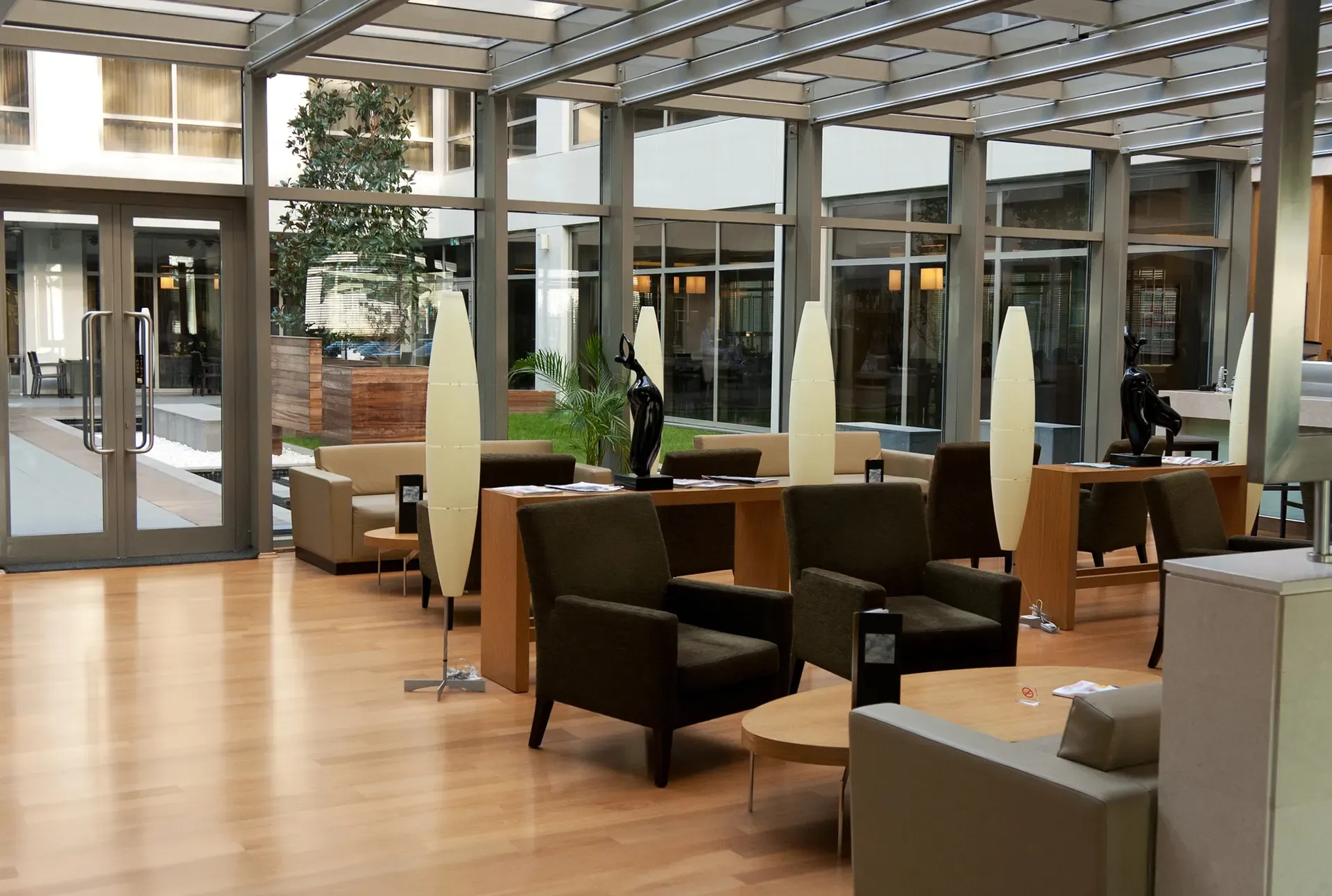 Lobby with seating areas, wooden floors, glass windows, and tall, slender lamps.