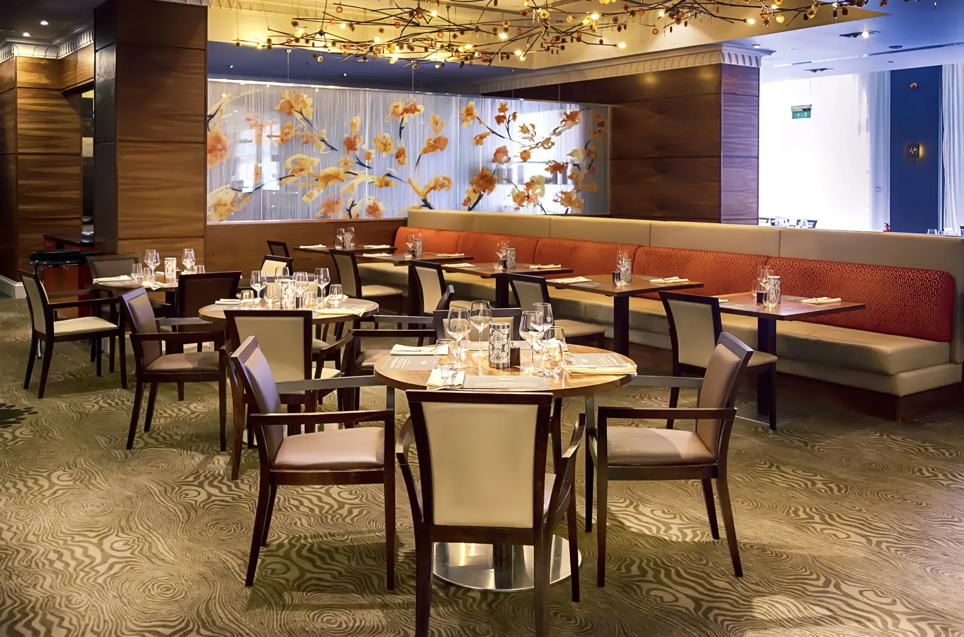 Upscale restaurant dining room with round tables, chairs, and a floral decor backdrop.