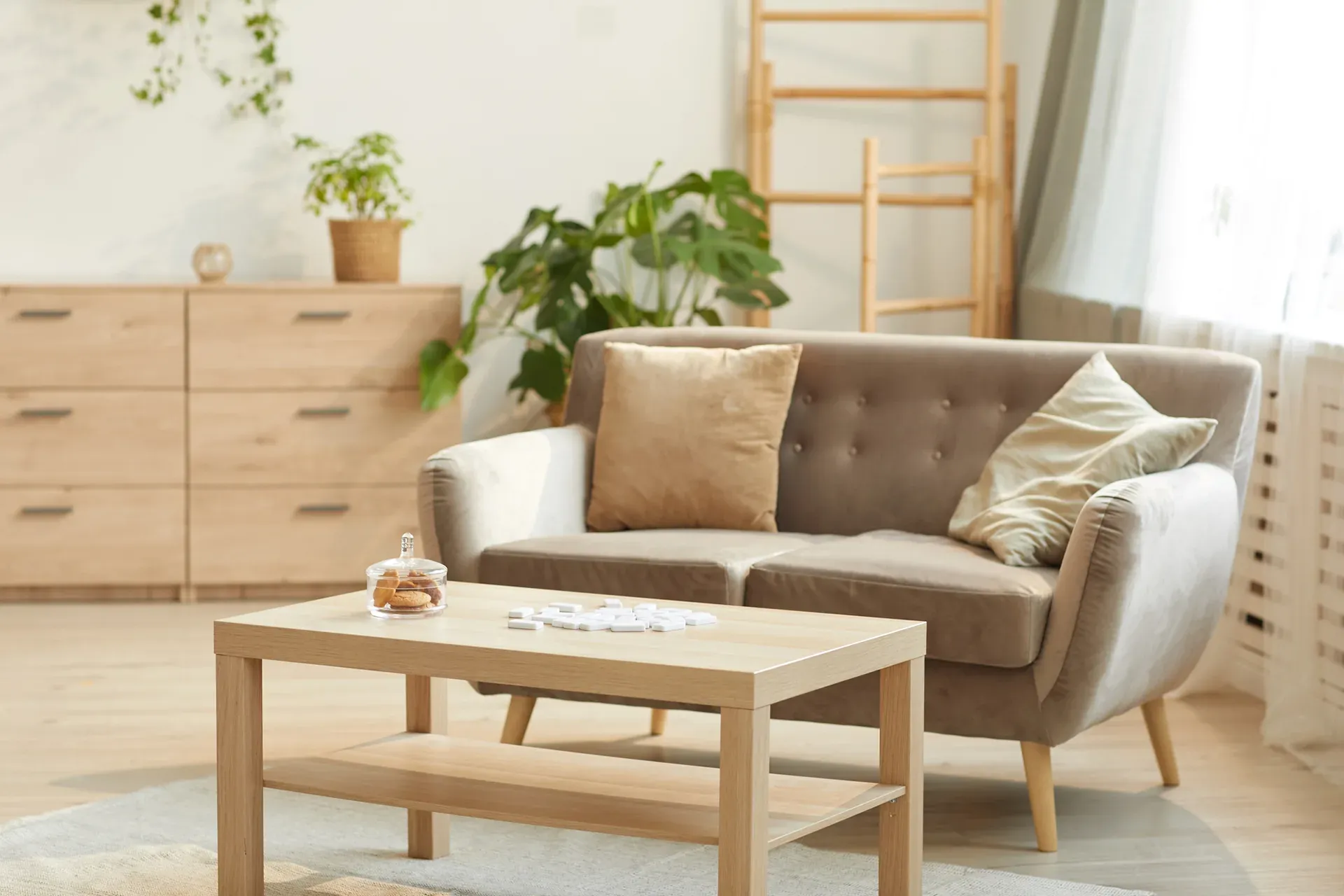 Living room with a tan sofa, wooden furniture, and plants, creating a cozy, well-lit space.