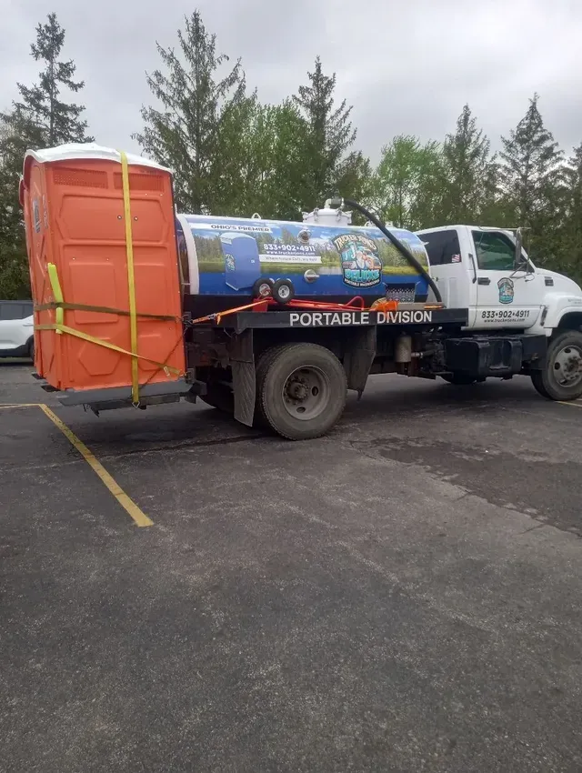 Trucker Jon’s portable restroom service truck transporting an orange portable toilet for delivery.