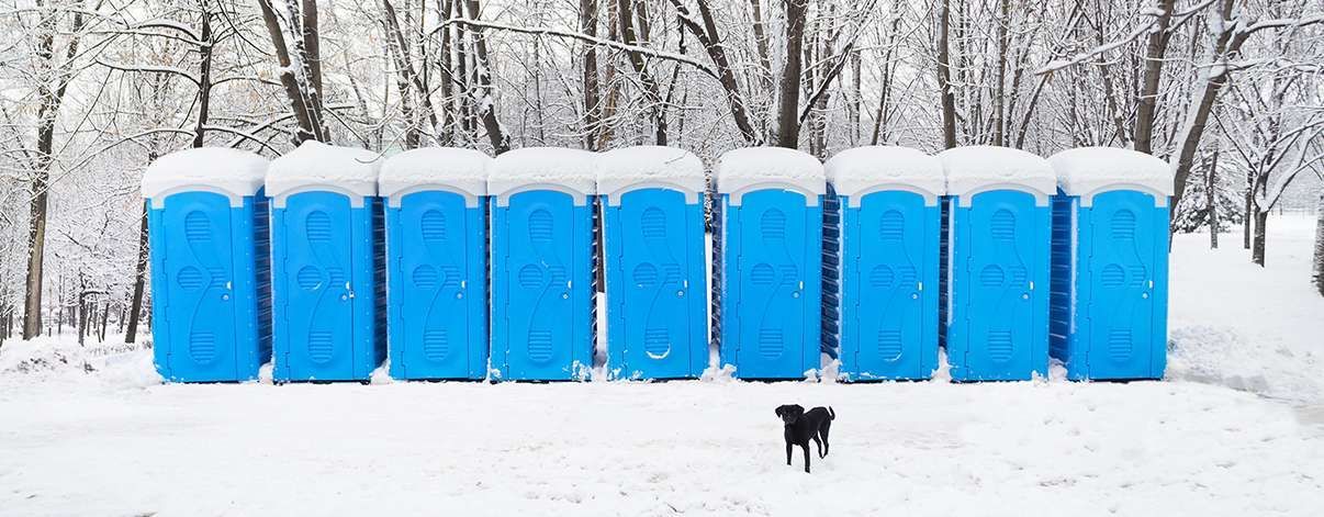 Row of blue portable toilets covered in snow during freezing winter temperatures at an outdoor location.