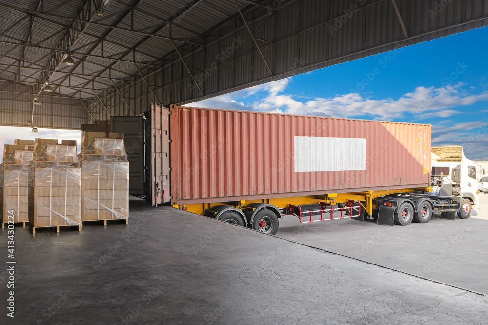 A truck is loading a shipping container into a warehouse.