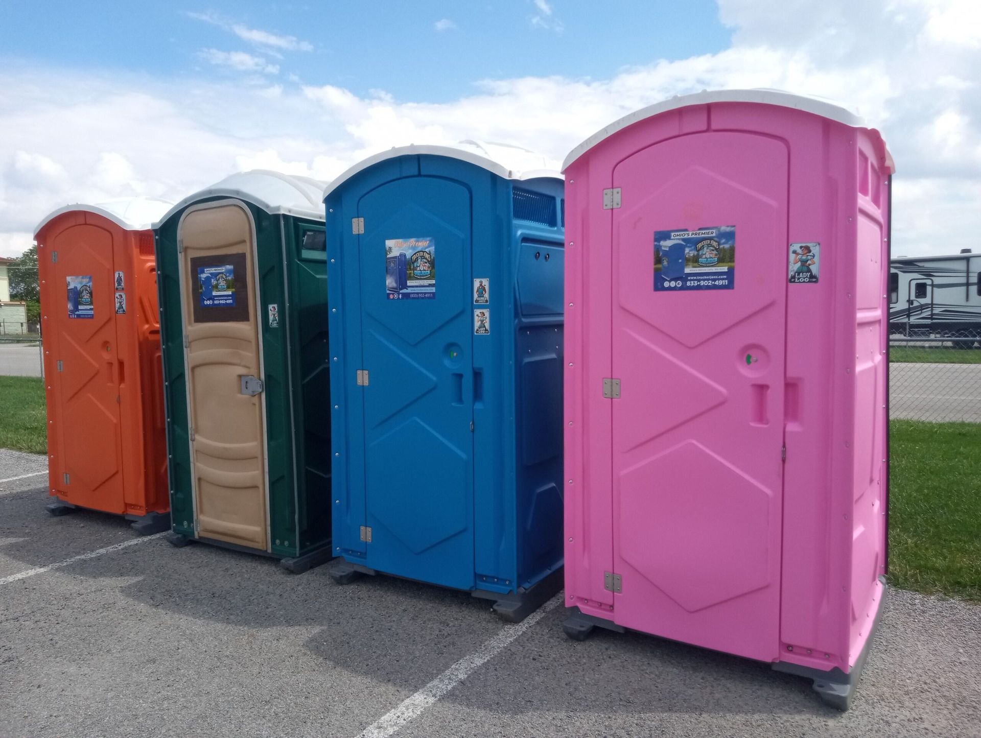 Row of colorful portable toilets lined up outdoors, including orange, tan, blue, and pink units.