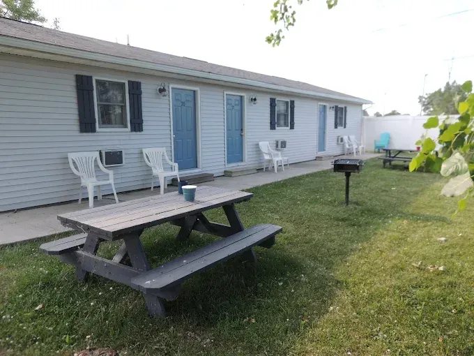 Backyard with picnic table, white chairs, blue doors, and a grill beside a house