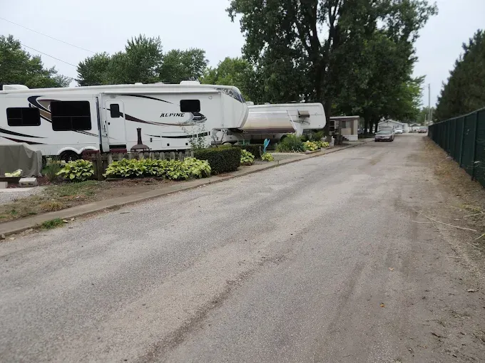 RVs parked along a gravel road beside a chain-link fence and tall trees
