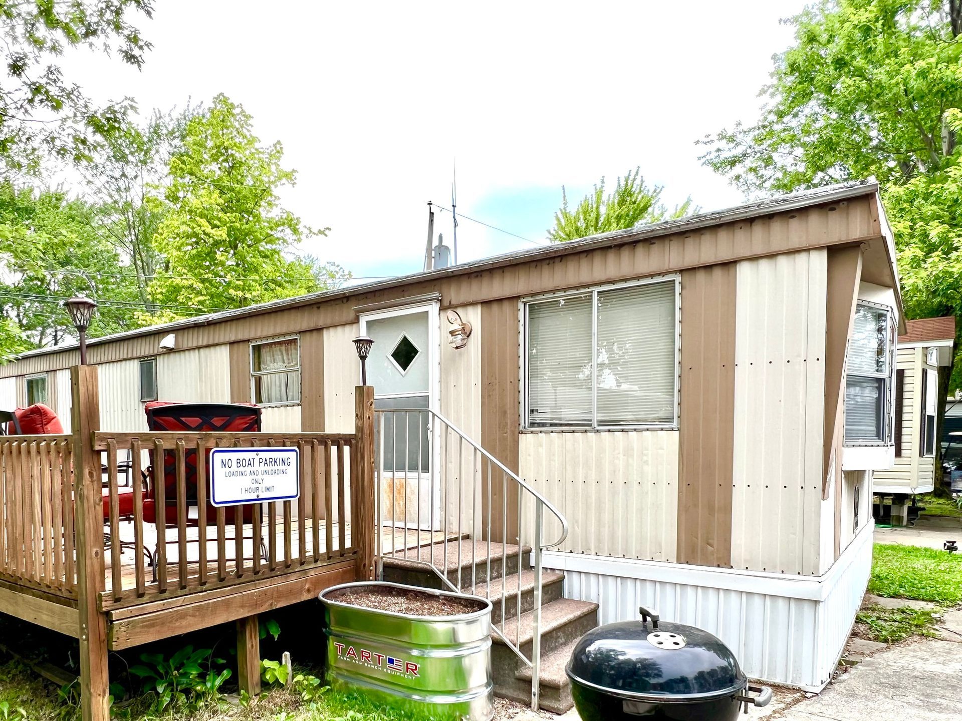 Mobile home with small wooden porch, steps, and a grill in front of trees