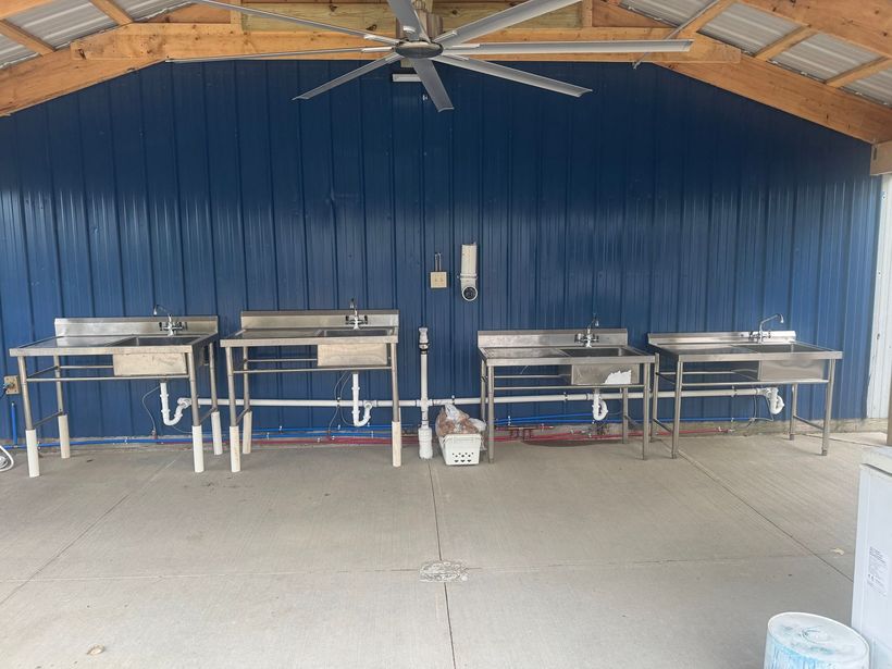 Outdoor shelter with blue wall, metal tables, and a ceiling fan over a concrete floor