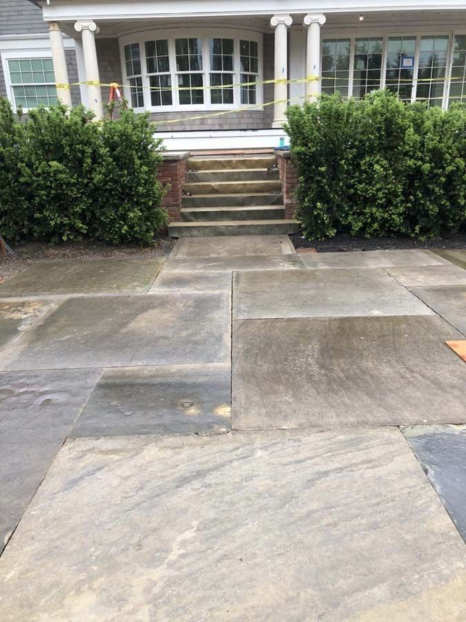 Exterior view of a house with stone pathway and steps leading to the front door, flanked by green bushes.