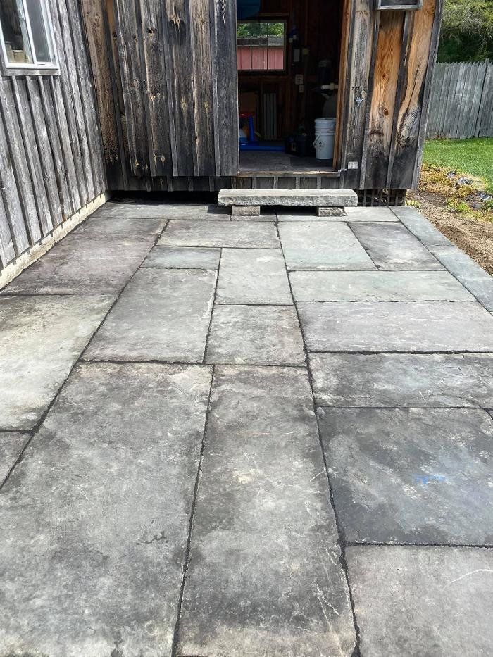 Stone patio in front of a weathered wooden building with an open doorway.
