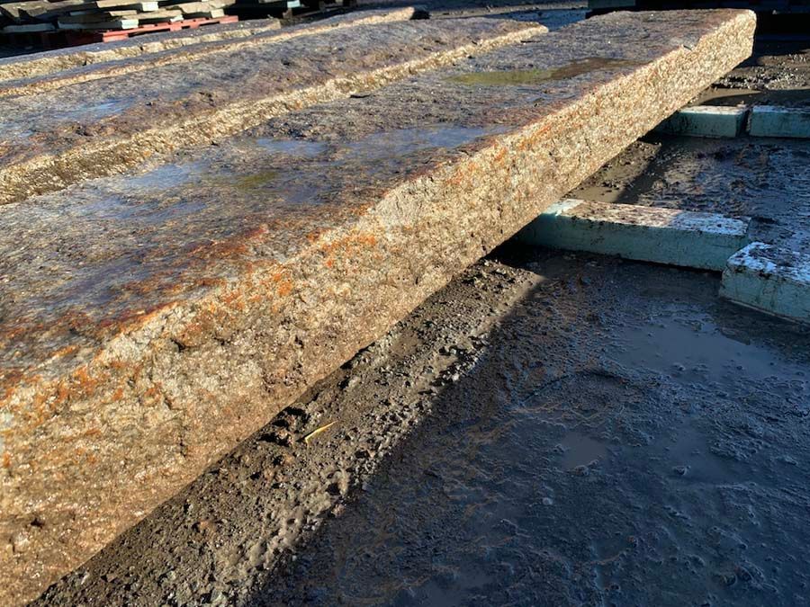 Concrete planks stacked outdoors, gray and weathered, resting on foam blocks.