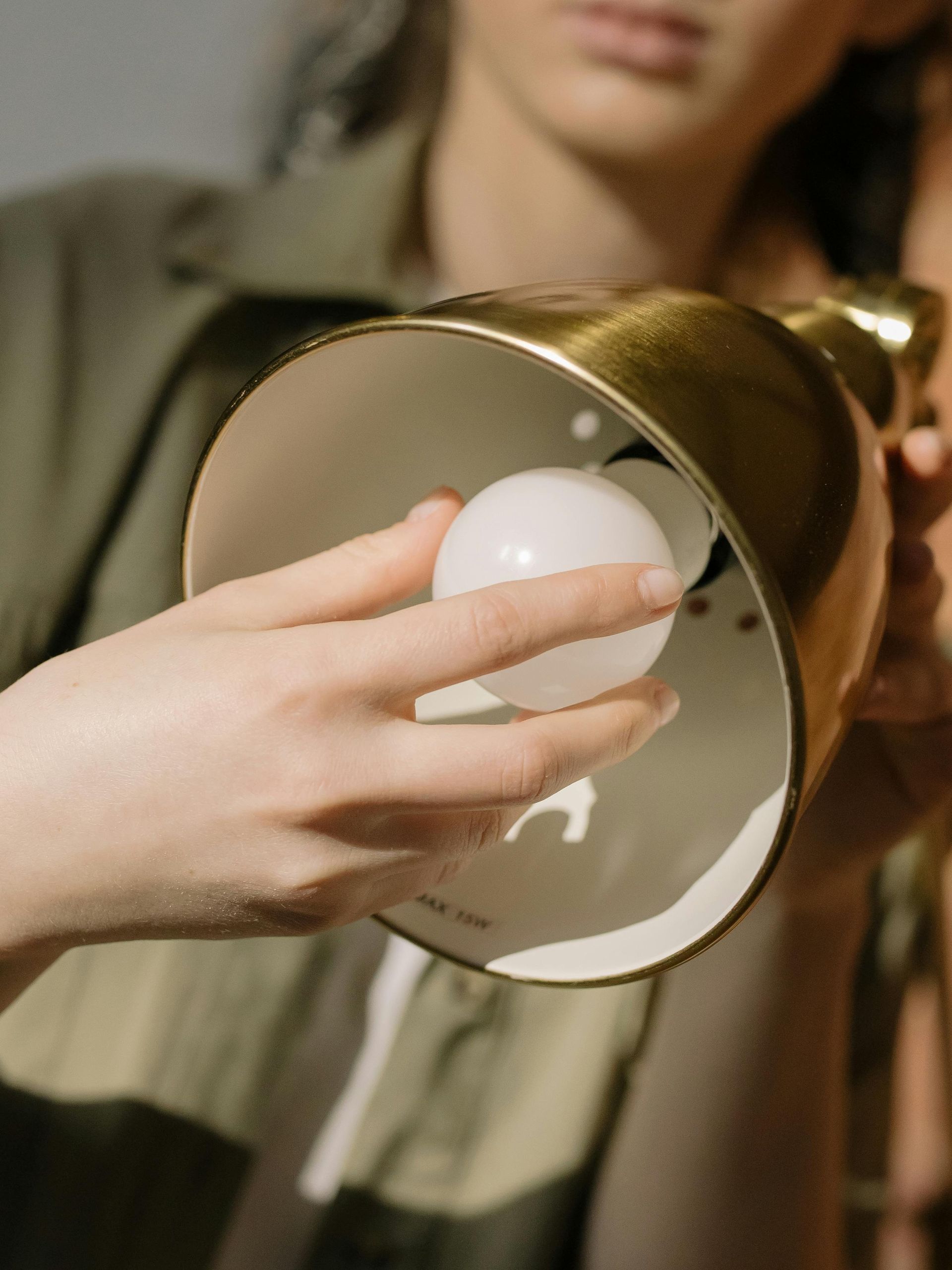 Person replacing a lightbulb in a brass lamp.