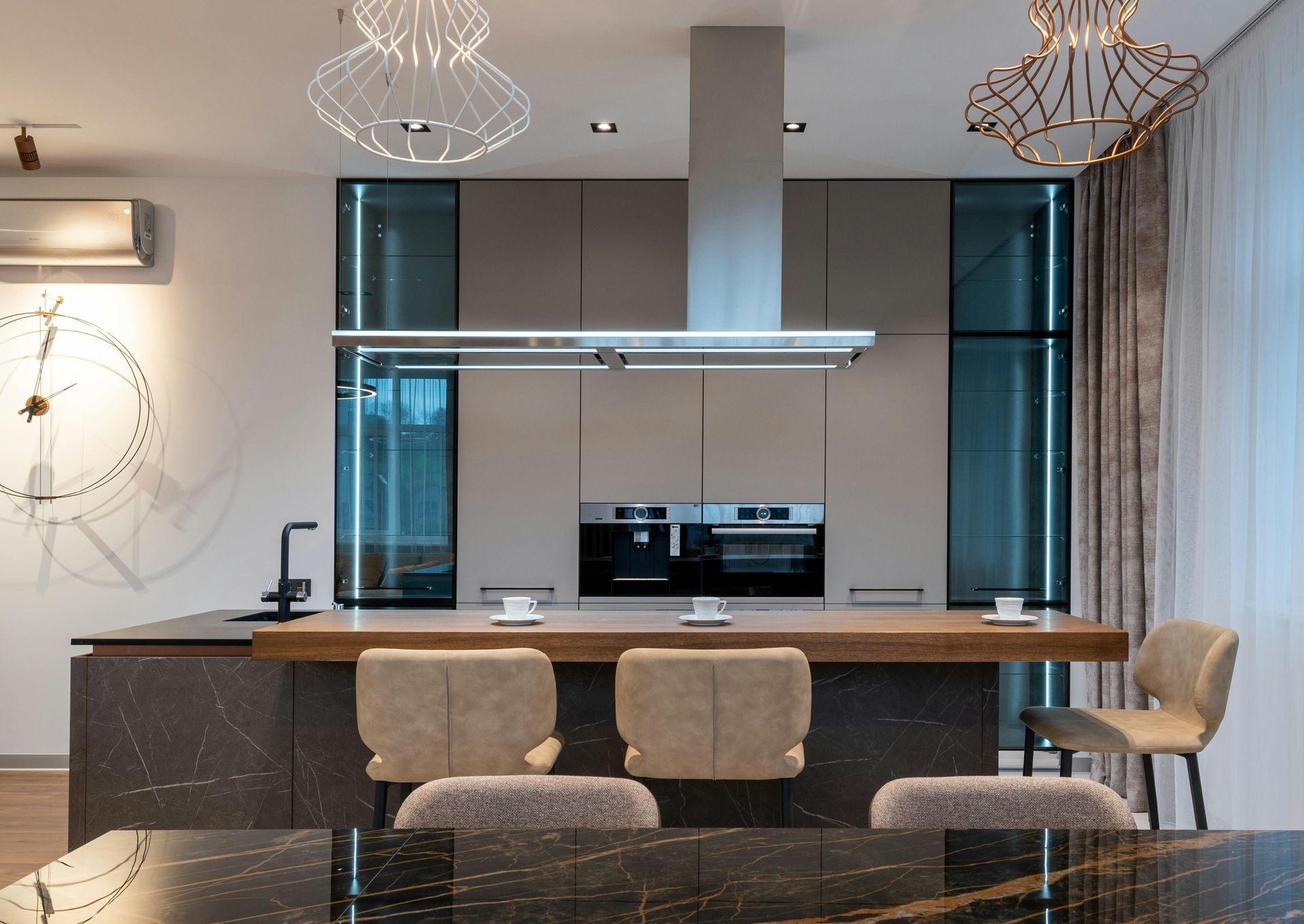 Modern kitchen with a gray and wood island, two ovens, and pendant lights.