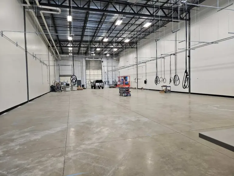 Large, empty warehouse interior with concrete floor and white walls. Overhead lighting and rigging visible.