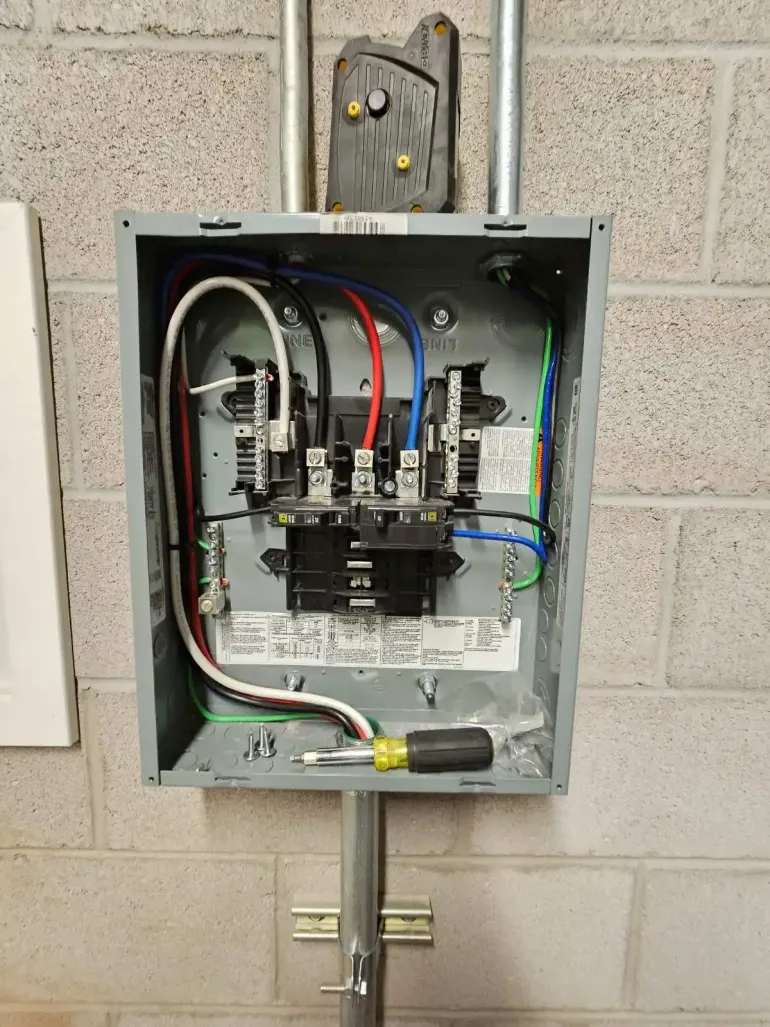 Electrical panel with wires and circuit breakers mounted on a brick wall, with a screwdriver inside.