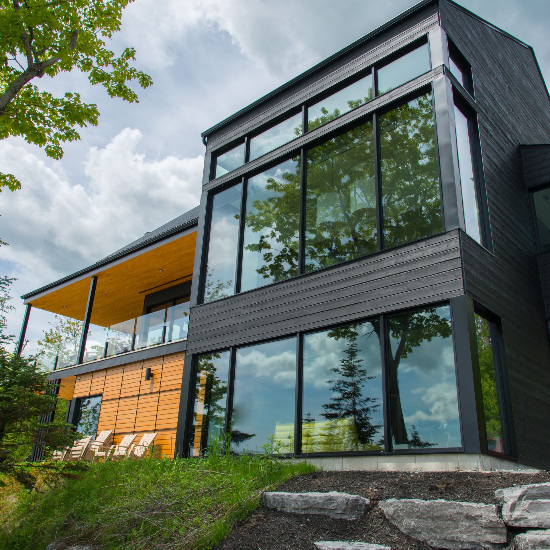 Modern black house with large windows, orange balcony, and stone steps on a grassy hillside