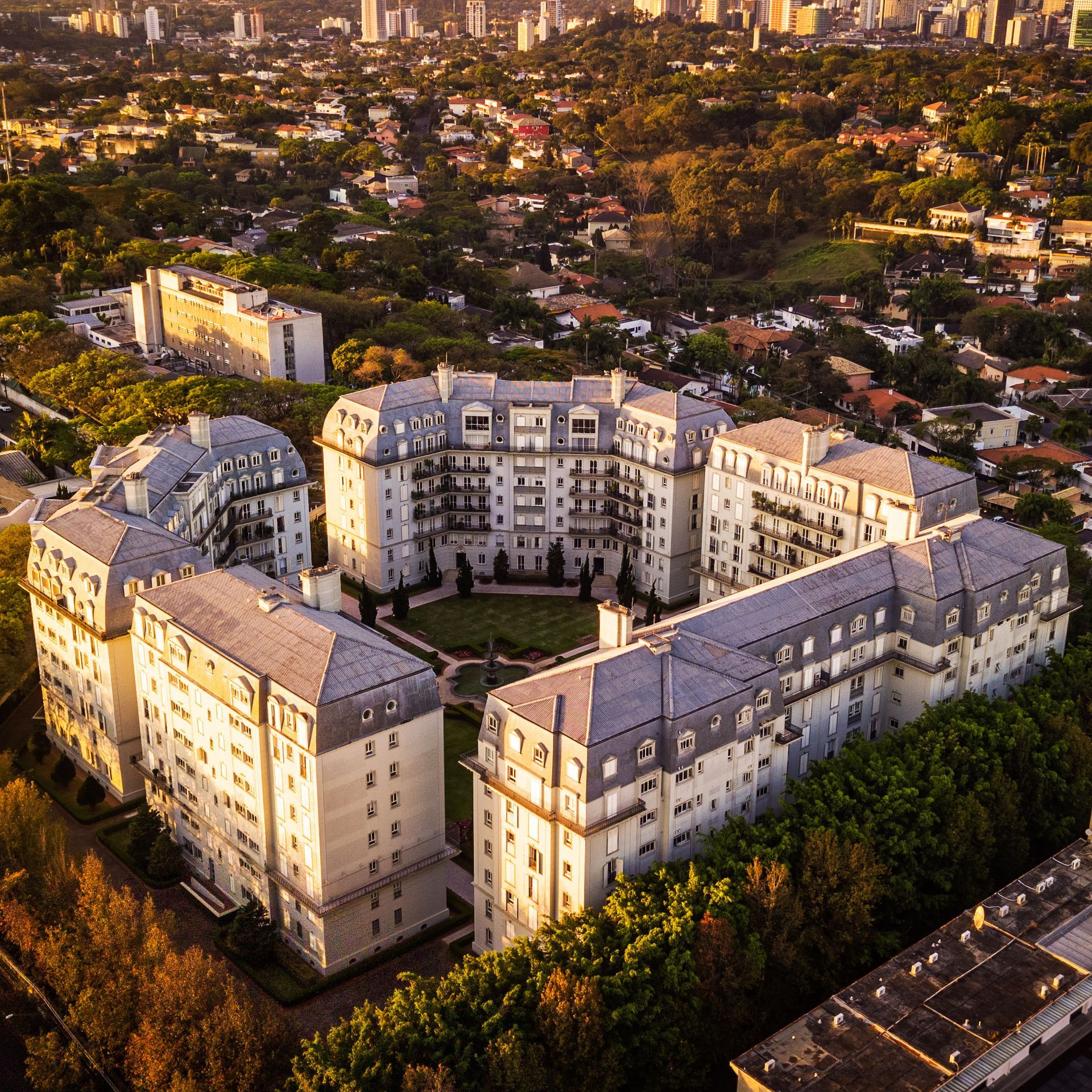 Aerial view of a large cream apartment complex surrounding a central courtyard in a city at sunset
