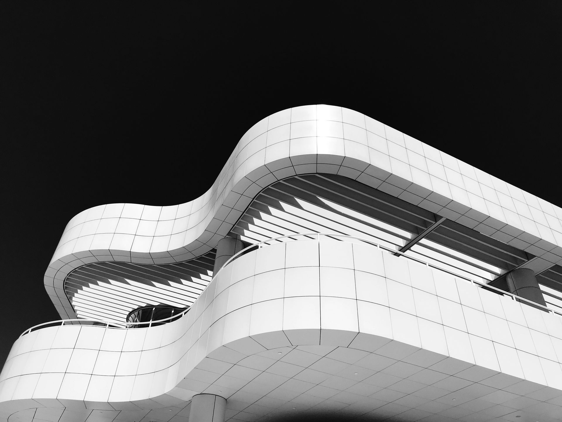 Modern white curved building facade against a black sky, viewed from below