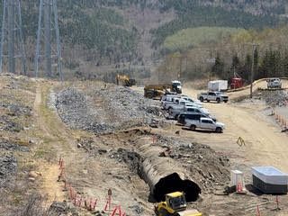 Construction site with trucks and equipment on a dirt road beside a large tunnel opening