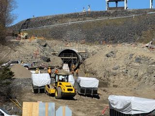 Construction site with a tunnel entrance in a rocky hillside and yellow machinery below