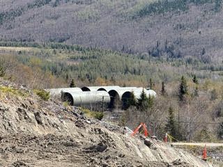Excavator working on a dirt slope near a bridge in a wooded mountain landscape