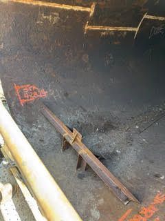 Rusty metal pipe inside a dark industrial container or tank with debris on the floor