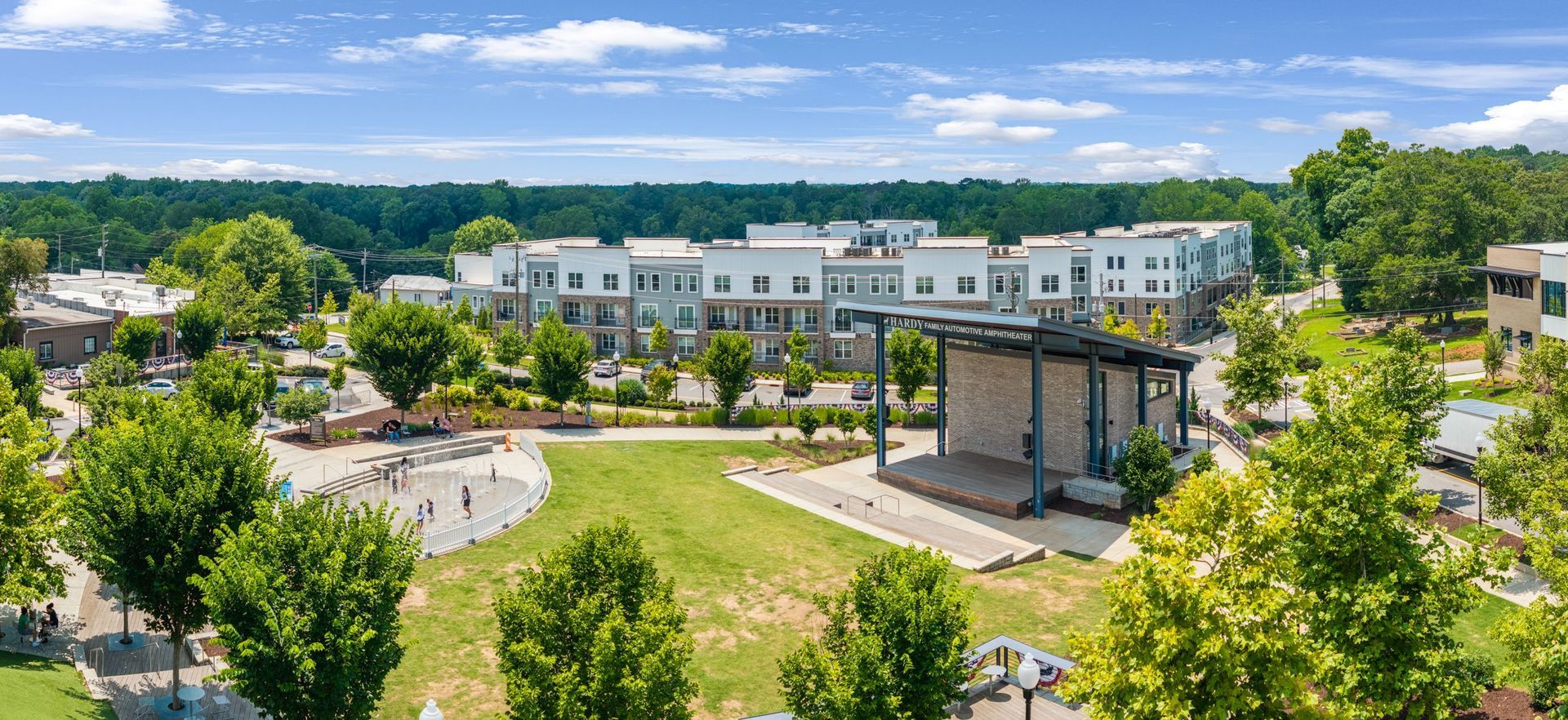 Aerial view of a modern apartment complex with a central green courtyard and amphitheater seating under a blue sky