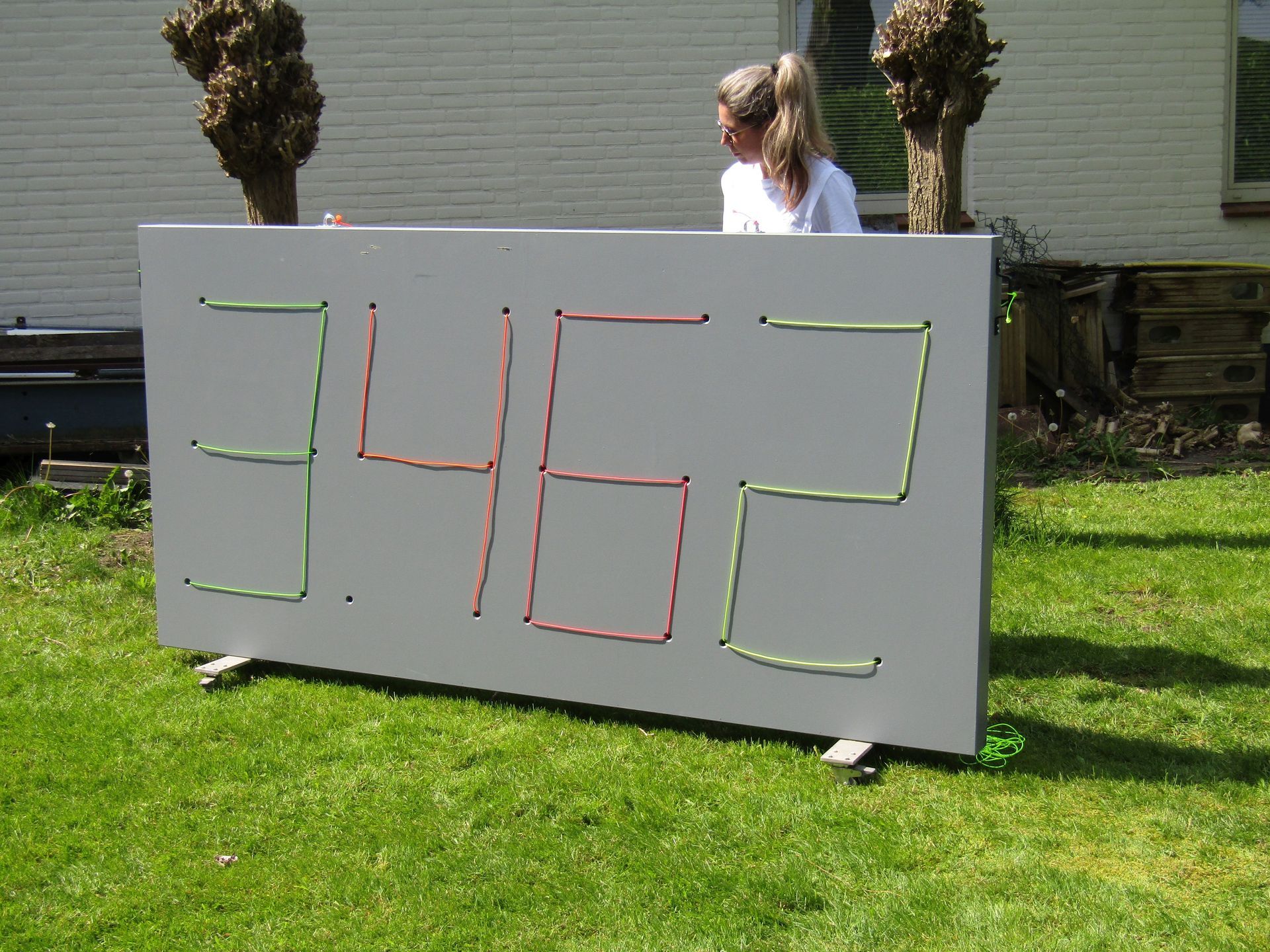 Een groot scorebord met groene en rode cijfers op een gazon, met een persoon op de achtergrond.