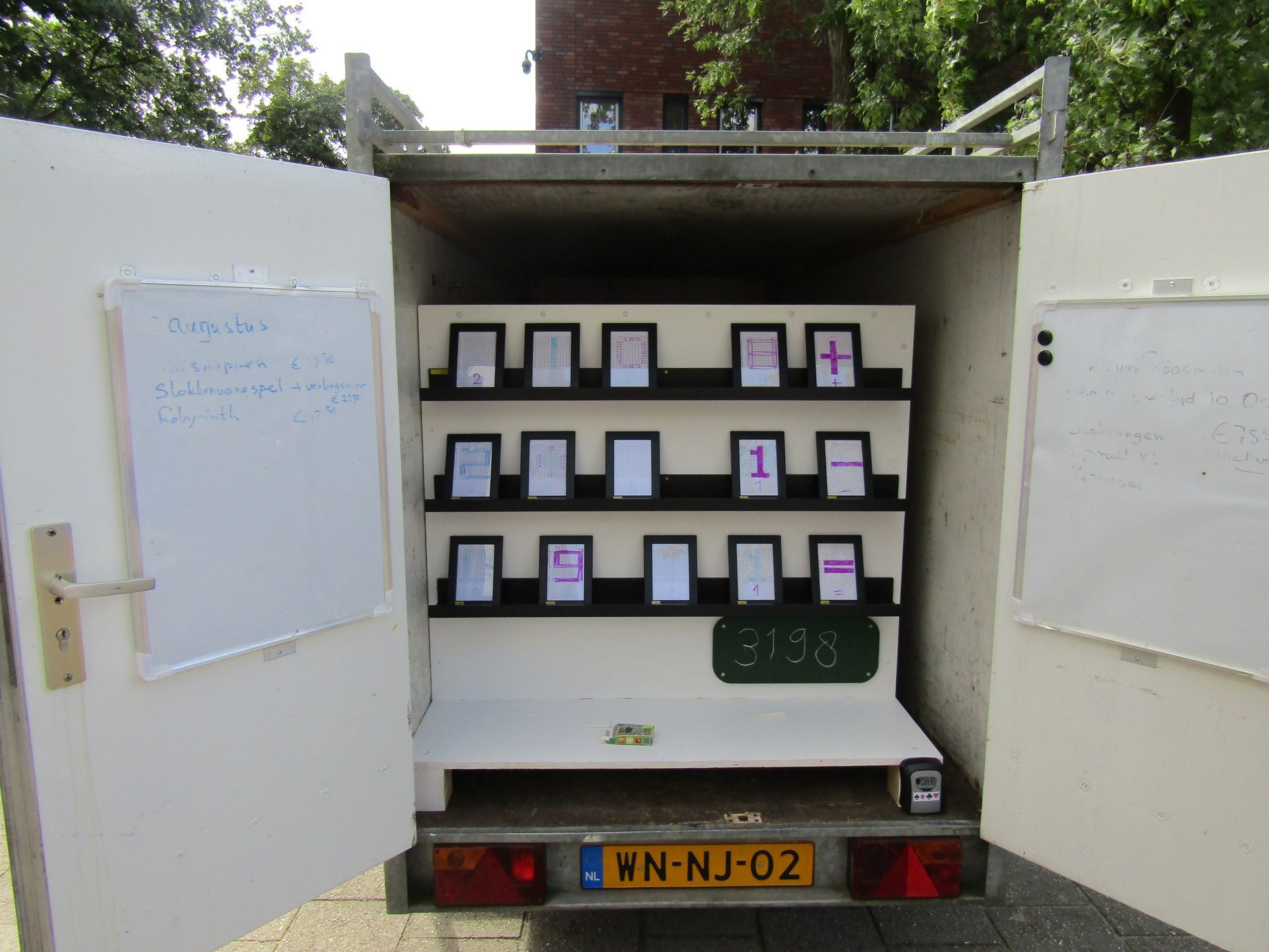 Open interieur van de trailer met planken waarop kleine ingelijste bordjes staan; op elke deur bevindt zich een whiteboard.