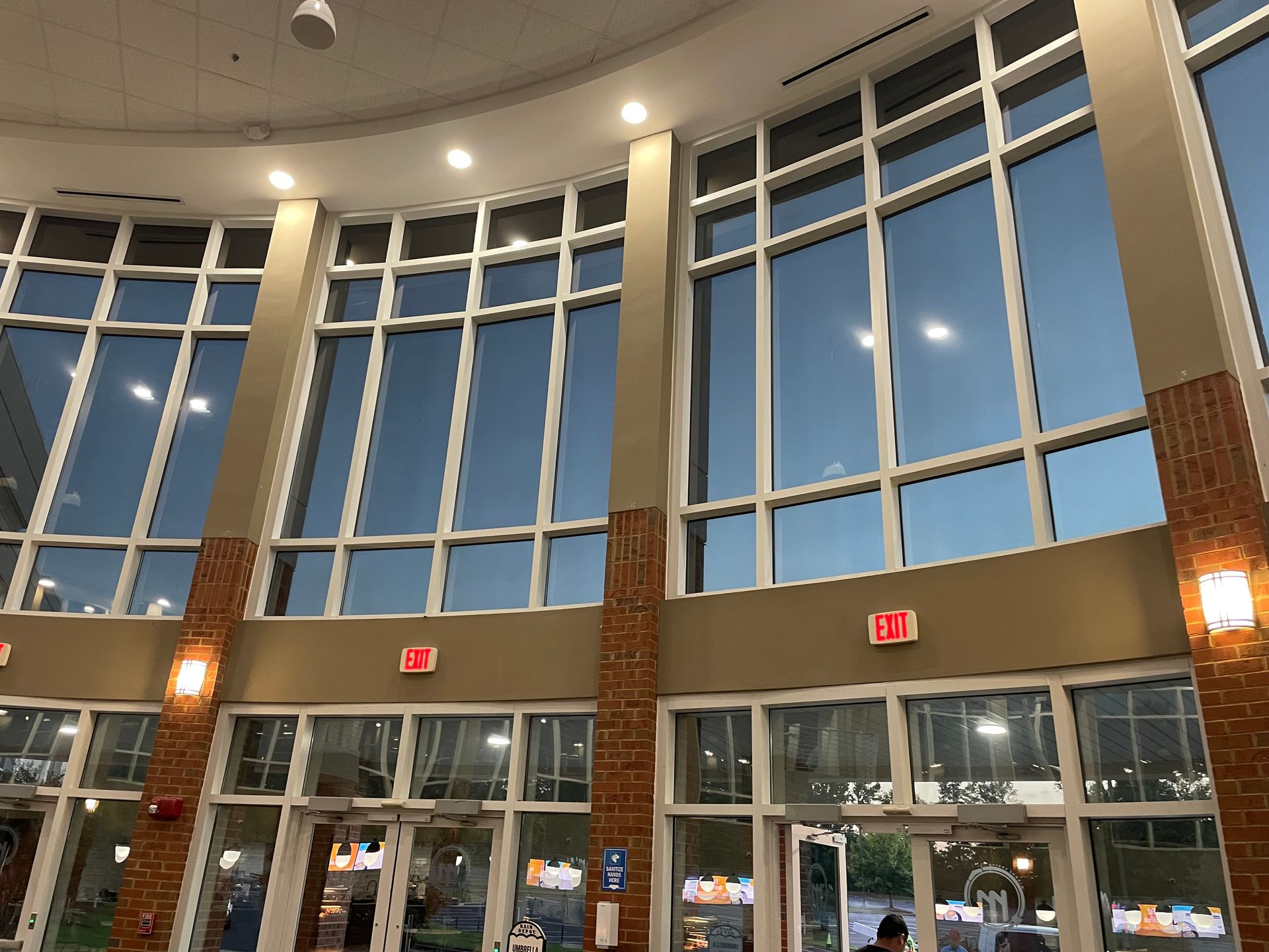 Tall lobby with large curved windows, glass doors, and warm wall lights at night