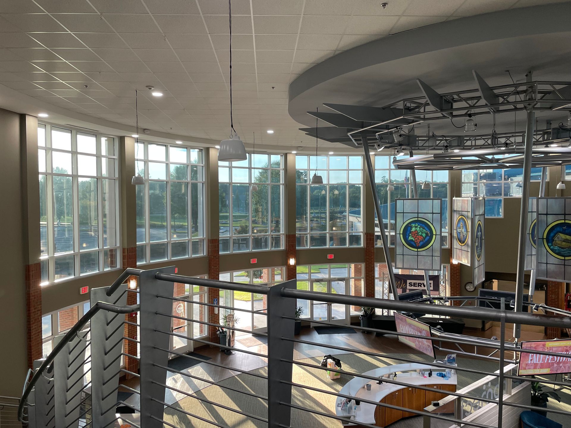 Modern atrium with floor-to-ceiling windows, central spiral stair, and colorful hanging circular art installation