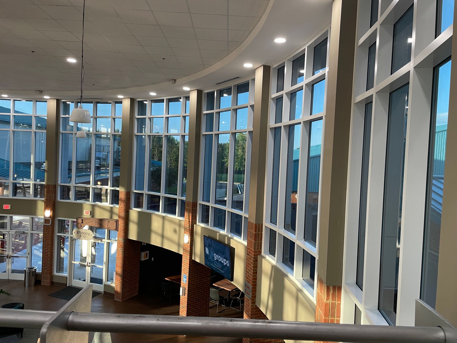 Curved lobby with tall glass windows, white columns, and warm wood seating overlooking outdoors