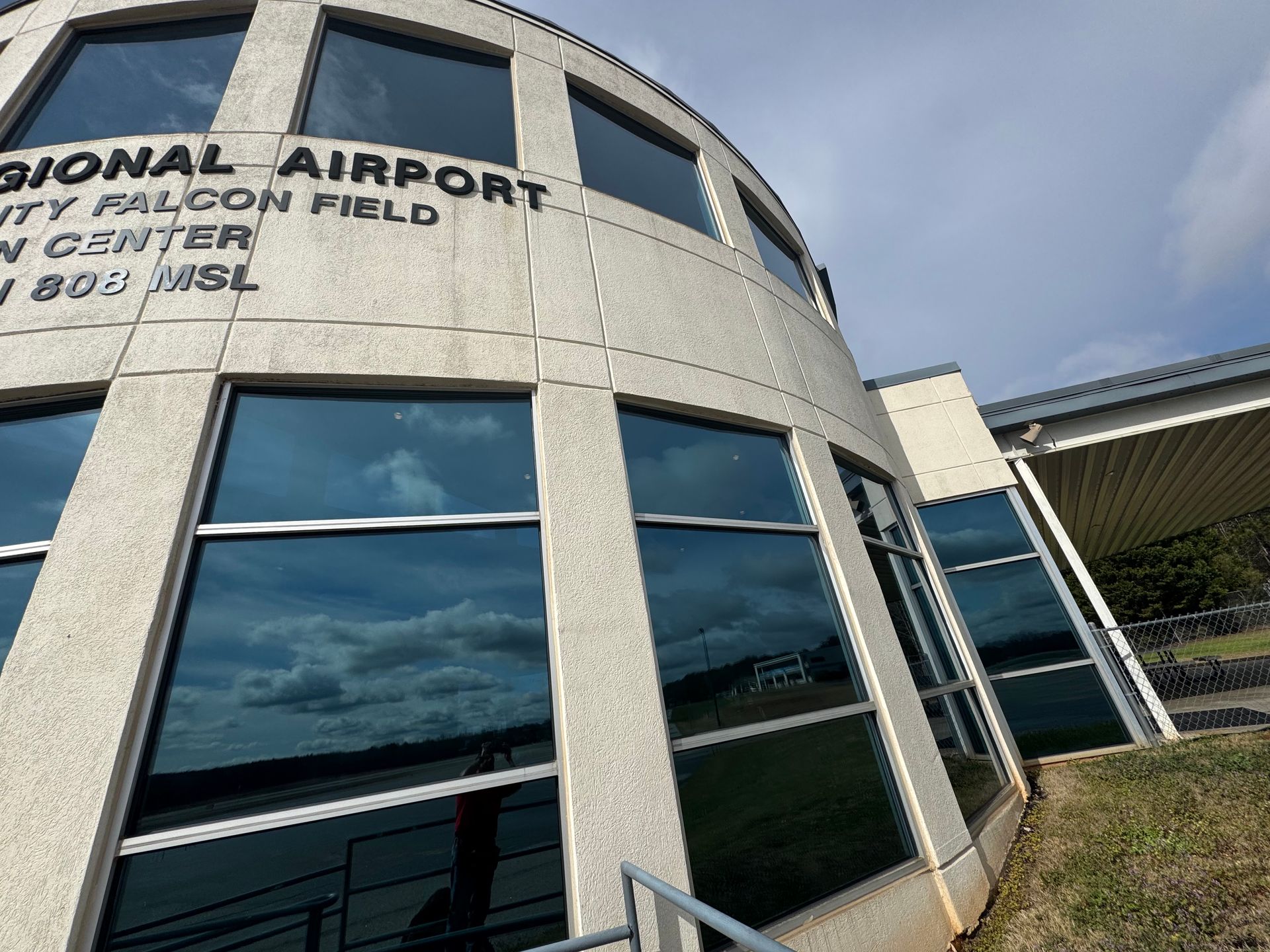 Regional airport terminal with reflective glass windows and a curved concrete facade under a blue sky