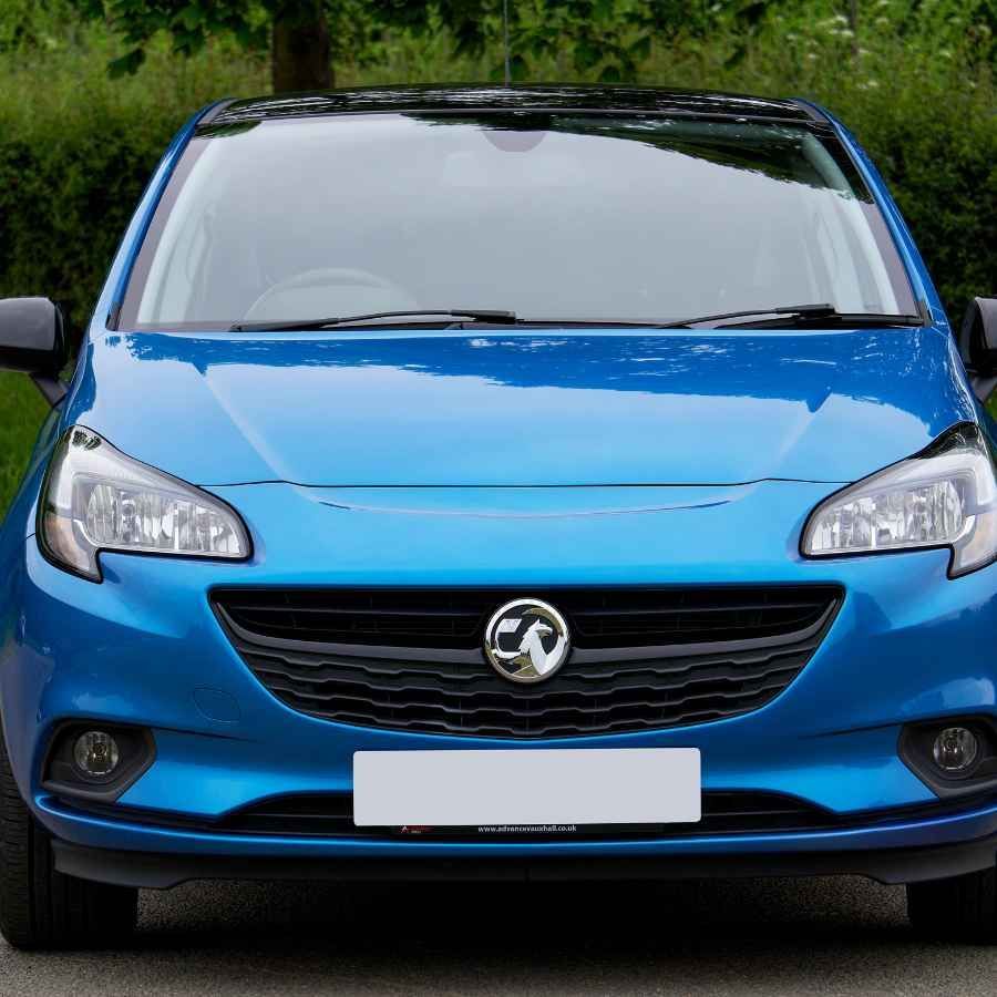 Blue compact car seen from the front on a road, with a blurred green background