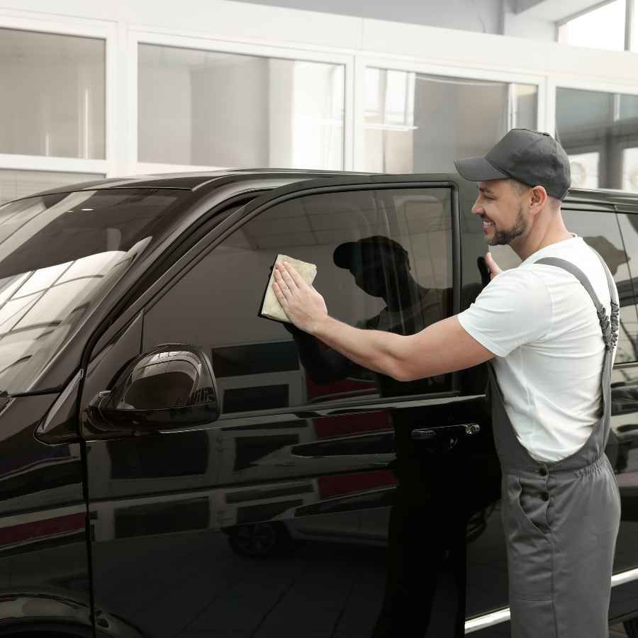 Man polishing a black car in a bright garage with a cloth