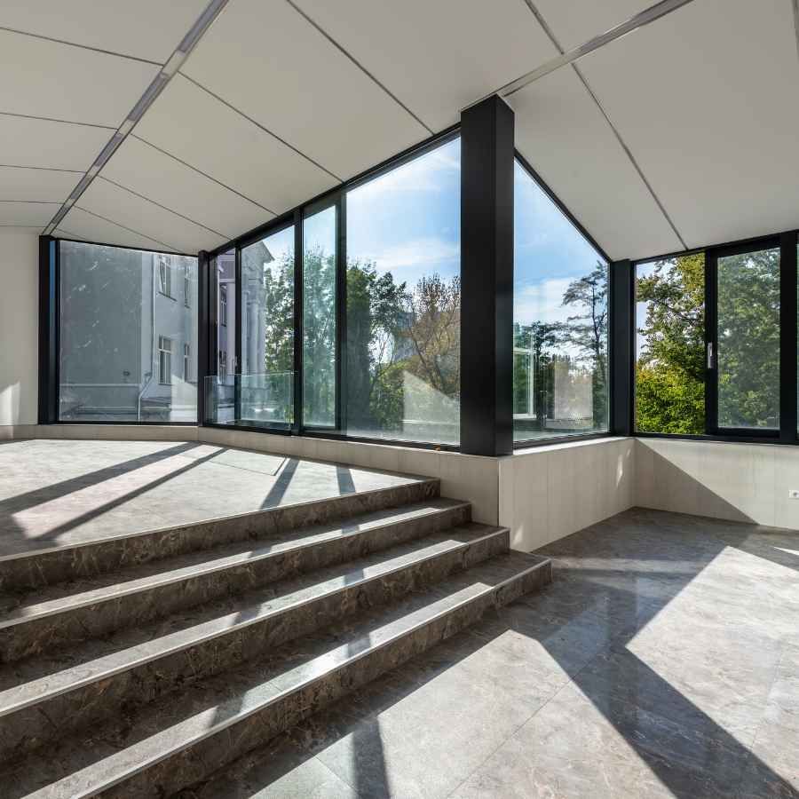 Sunlit indoor stair landing with large glass windows and gray stone flooring