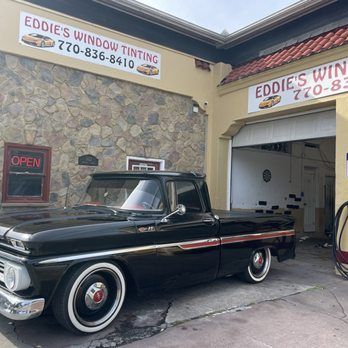 Classic black vintage pickup outside Eddie’s Window Tinting shop, with a stone wall and open garage bay.